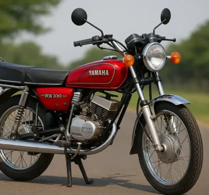 Yamaha RX 100 red vintage motorcycle with chrome exhaust and round headlamp parked on a road with trees in the background